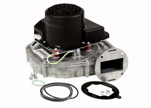 An angled professional studio shot from image_8e2007.jpg of a Weil-McLain combustion blower kit, showcasing the cast-aluminum fan scroll body, integrated black cylindrical motor top-block, and the rectangular exhaust flue flange port alongside an included circular replacement gasket pack isolated on a black background.